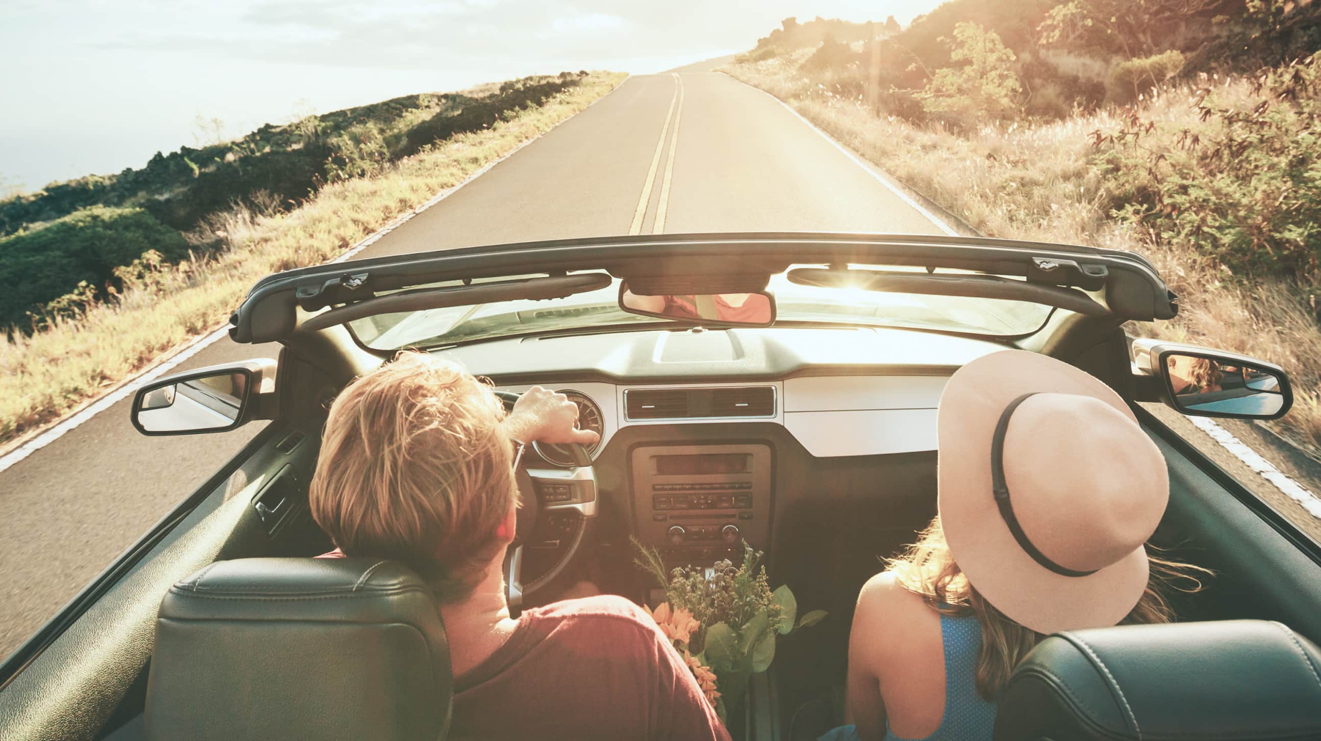 Rear view from inside a car of two people driving along a coastal road.