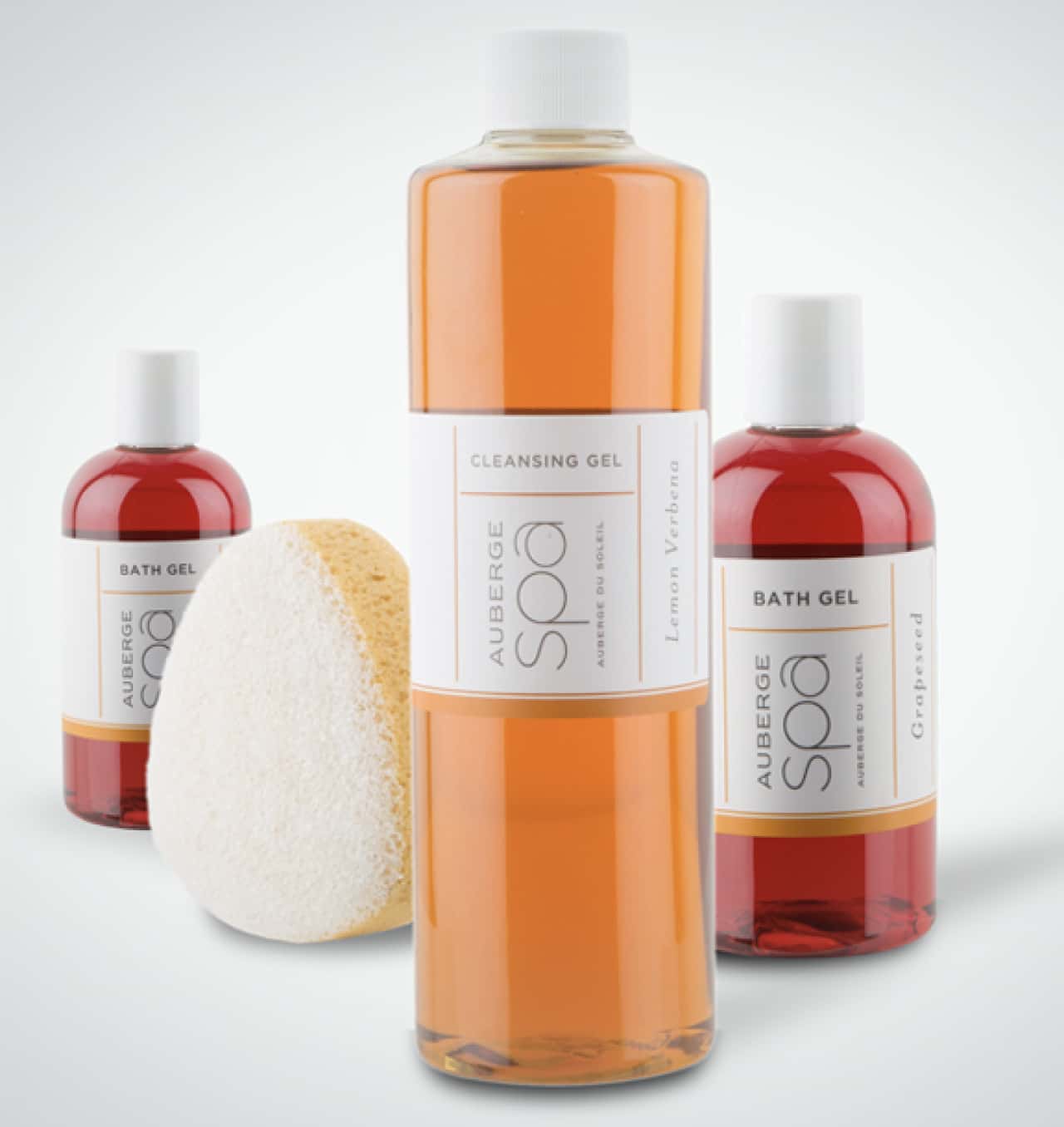 Three spa products labeled 'Auberge Spa' including a cleansing gel and bath gel, alongside a natural sponge, against a white background.